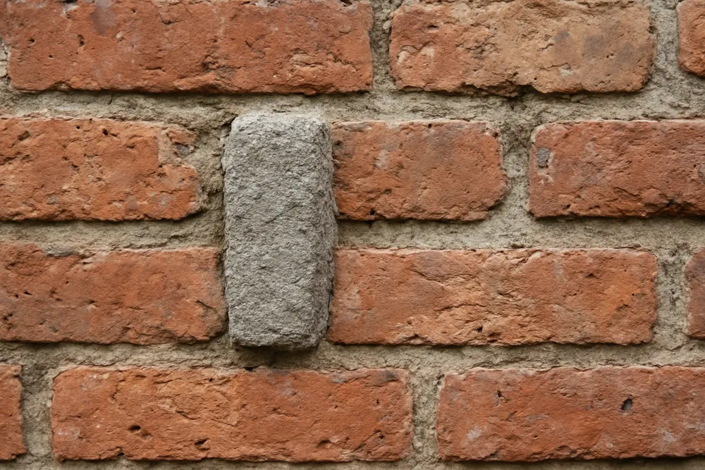 A hard grey mortar joint standing proud of a worn soft brick — cement, render and paint on old walls, Adelaide. Illustrative example.